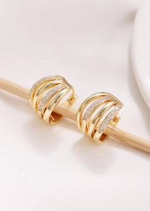 Detalle de pendientes de aro dorados multicapa con micropavé de circonitas sobre seda blanca