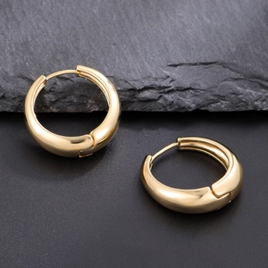 Boucles d'oreilles créoles dorées à l'or 18 carats sur un fond en pierre naturelle gris foncé