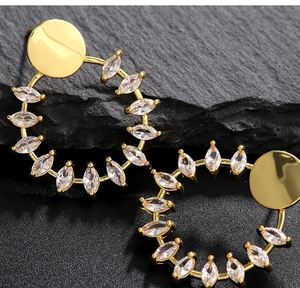 Detalle macro de pendientes de aro dorados con circonitas corte marquesa sobre fondo de pizarra