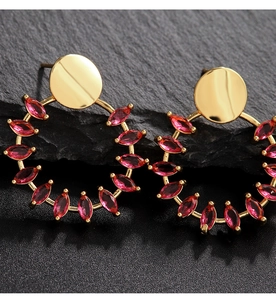 Primer plano de pendientes de aro dorados con circonitas rojas brillantes en corte marquesa