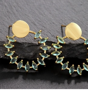 Primer plano de pendientes dorados con circonitas turquesas de corte marquesa sobre piedra