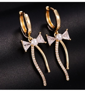 Détail de boucles d'oreilles nœud dorées avec perles, zircons et pampilles
