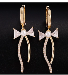 Détail de boucles d'oreilles nœud dorées avec zircon, perle et pompons métalliques brillants