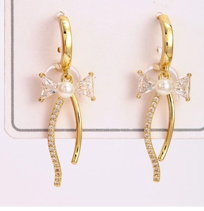 Détail de boucles d'oreilles nœud dorées avec perle blanche et longs pompons pendants