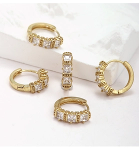 Detail shot of brass gold hoop earrings with three square-cut zircon stones on a marble base