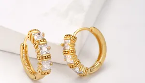 Macro view of gold brass huggie earrings with square zircon and beaded texture edges