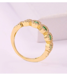 Detalle macro de anillo dorado con tres piedras verdes ovaladas y pavé de cristales