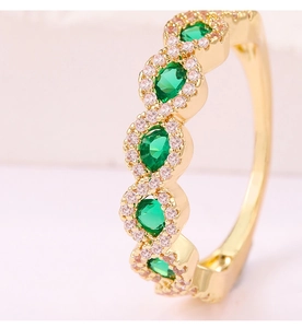Vista macro de anillo dorado ondulado con cinco circonitas verdes ovales y detalles brillantes
