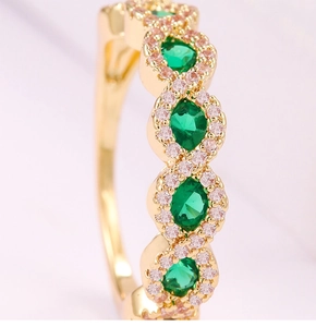 Detalle macro de anillo dorado con esmeraldas verdes ovaladas y halo de circonitas rosas