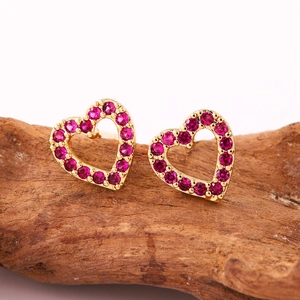 Nahaufnahme herzförmiger Goldstecker mit rosa Zirkonia auf rustikalem Holzständer