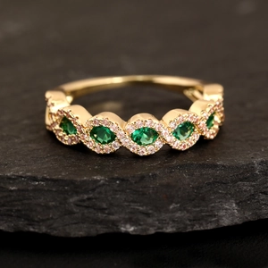 Anello con zirconi verde smeraldo micro-pavé e fascia dorata su sfondo in pietra nera