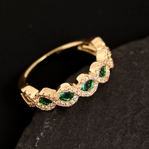 Macro dettagliata di un anello ondulato in oro con zirconi verde smeraldo incastonati