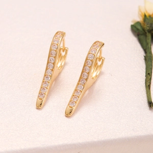 Macro shot of gold-plated hoop earrings with sparkling cubic zirconia on a white texture