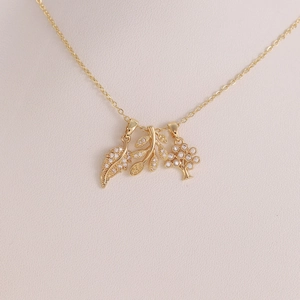 Dettaglio macro della collana d'oro con ciondoli a foglia e albero in zirconi su busto