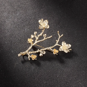 Elegant gold-plated plum blossom branch brooch accessory on a textured black background