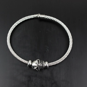 Macro view of steel cable bangle featuring a detailed skull charm and metal beads
