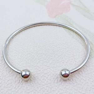 Dettaglio di un bracciale a rigido in acciaio inossidabile lucido a forma di C con sfere