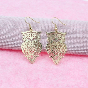 Detailed close-up of rose gold owl earrings with intricate filigree cut-outs
