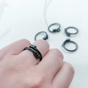 Détail d'une bague en câble d'acier noir industriel avec un design torsadé à double couche