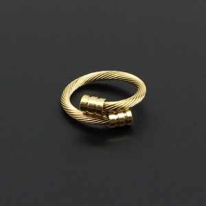 Détail macro d'une bague câble torsadée dorée avec embouts cylindriques sur fond noir