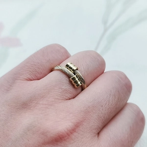 Gros plan sur une bague ouverte torsadée dorée portée sur une main féminine