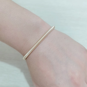 Nahaufnahme eines goldenen Federarmbands aus Gitarrensaiten am Handgelenk