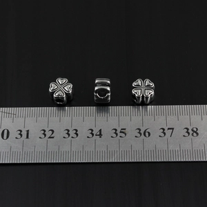 Macro shot of clover heart stainless steel beads with ruler showing 10mm size