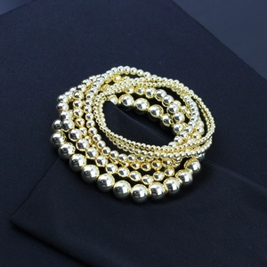 Dettaglio di braccialetti elastici con perline placcati oro 14K su tessuto blu scuro