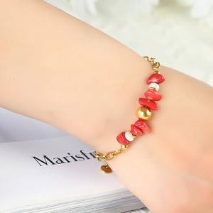 Bracciale a catena in acciaio dorato con pietre rosse e perle bianche indossato al polso