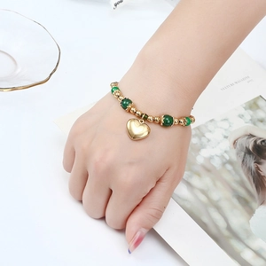 Bracelet de perles dorées et agate verte avec pendentif cœur porté sur le poignet
