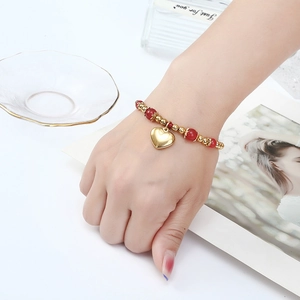 Détail du bracelet en perles dorées avec perles rouges et pendentif coeur au poignet
