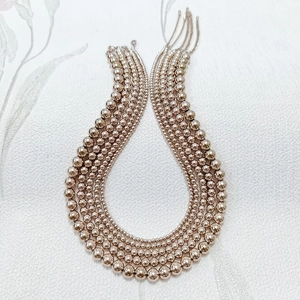 Polished rose gold beaded necklace set with various ball sizes on floral background