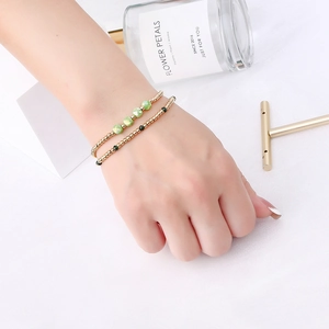Detail of waterproof gold beaded bracelets with faceted light green crystals on white fabric