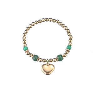 Bracelet à perles dorées avec pierres vertes et grand pendentif en cœur sur fond blanc