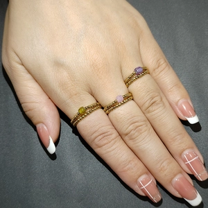 Close-up of three elastic gold bead rings with green, pink, and purple gemstones on hand