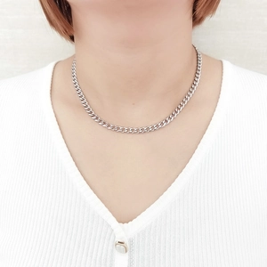Collier classique à mailles cubaines argentées en acier porté sur un pull blanc à col en V