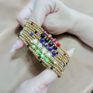 Detailed view of layered golden bead bracelets with colorful faceted crystals on wrist