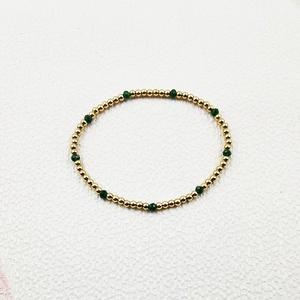 Detailed shot of handmade beaded bracelet with gold beads and faceted green crystals