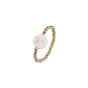 Macro shot of gold beaded elastic ring featuring a white shell disc with letter T engraving
