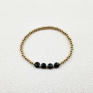 Detail of gold beaded bracelet featuring faceted black spinel stones on a white background