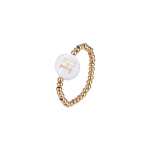 Macro detail of elastic gold beaded ring featuring a white shell charm with letter H