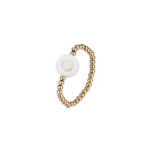 Detailed macro shot of a gold beaded elastic ring featuring a white shell charm with letter G