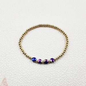 Close-up of golden beaded bracelet featuring four faceted purple and blue crystal charms