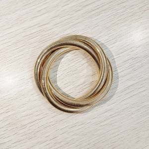 Detalle de brazalete de tres capas dorado con textura ondulada sobre fondo madera