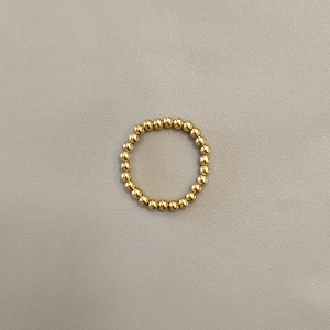 Detail shot of a minimalist gold stainless steel beaded ring on a textured grey background