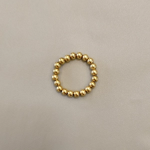 Macro shot of polished gold-plated stainless steel beaded elastic ring on grey leather