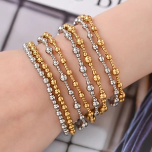 Stacked gold and silver stainless steel beaded bracelets on a wrist with metallic shine