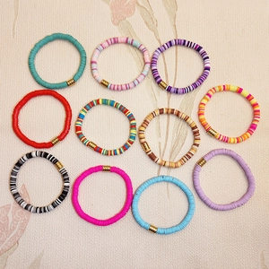 Macro shot of 11 colorful Heishi bead bracelets with gold accents and elastic bands