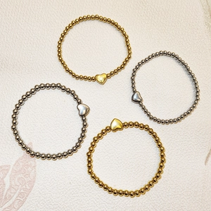 Dettaglio di quattro bracciali elastici a sfere oro e argento con ciondoli a cuore