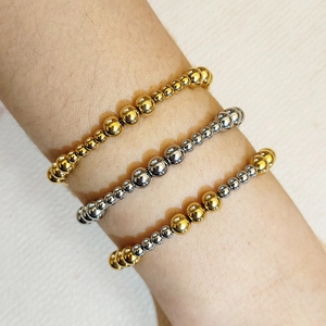 Primo piano di tre braccialetti con perline sovrapposti in oro e argento al polso